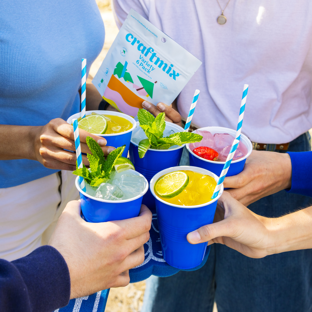 Group of friends smiling and enjoying Craftmix cocktails around a dining table with a Craftmix Variety Pack on display.