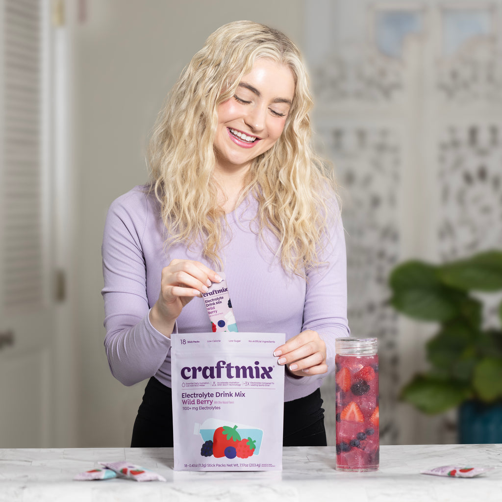 Woman using Craftmix Wild Berry Electrolyte Drink Mix stick packs with a glass of fruit-infused electrolyte water.